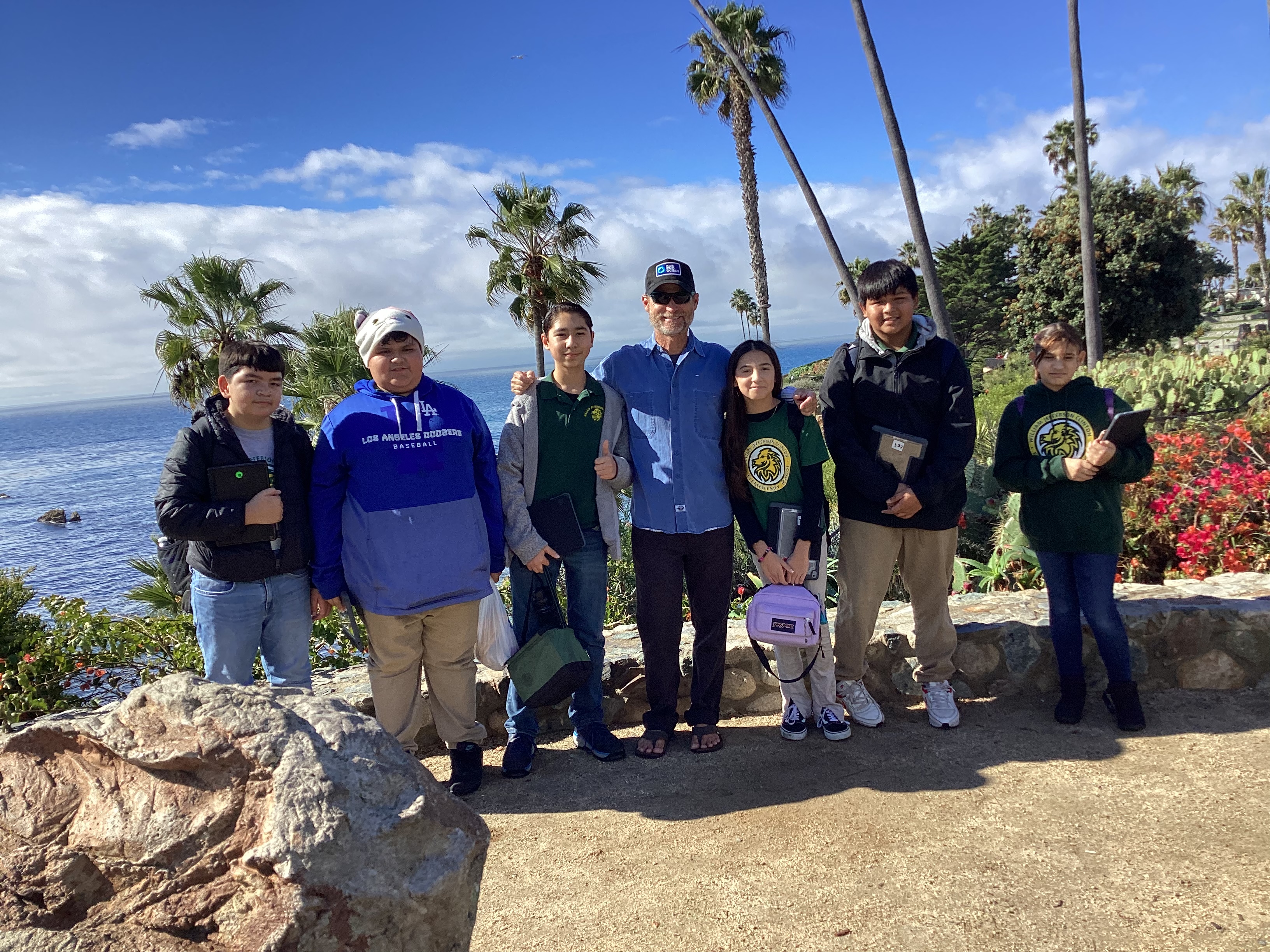 Rich German with students at scenic coastal overlook with ocean views and palm trees, educational field trip, outdoor learning experience