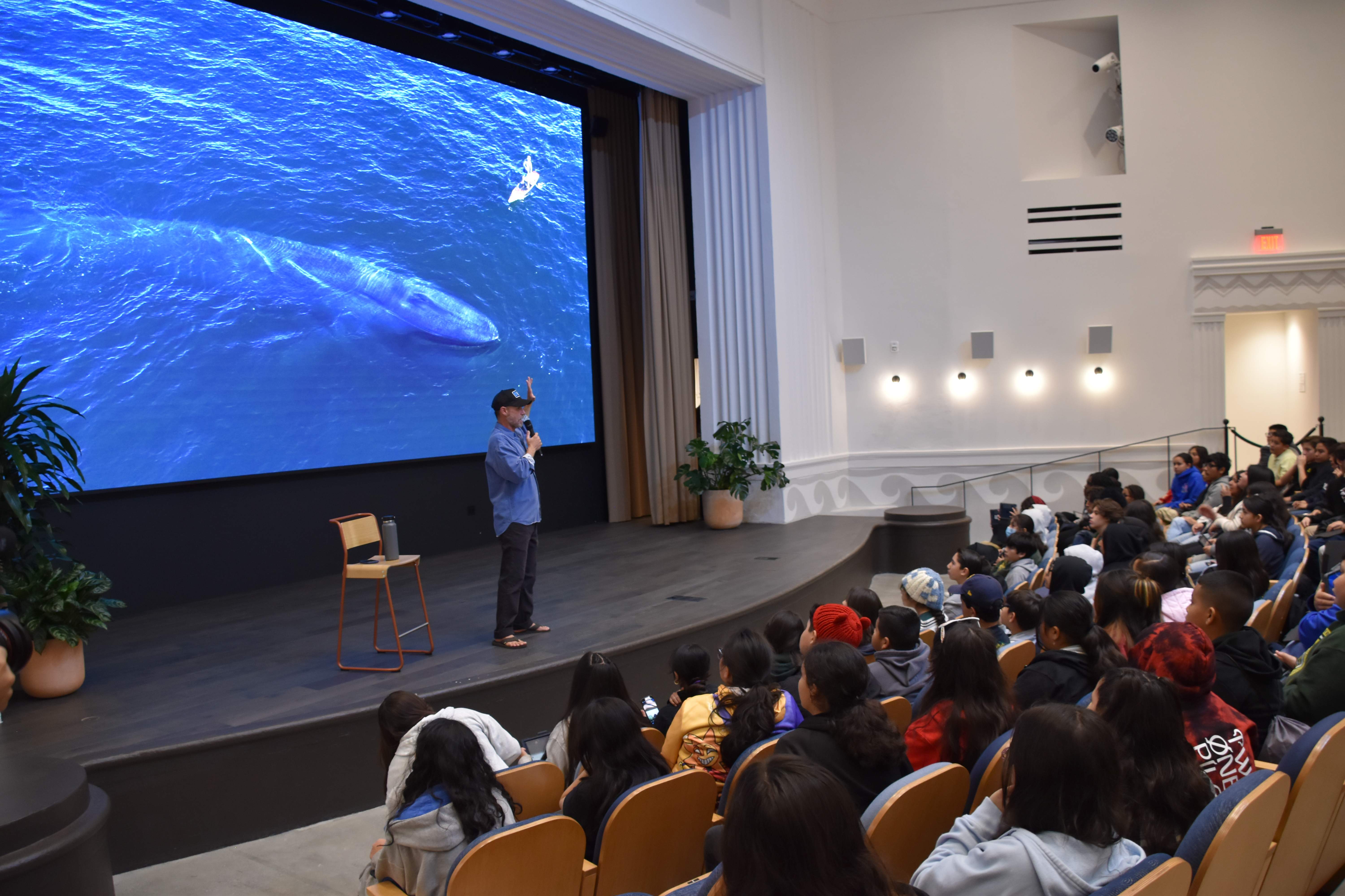 Rich German presenting to audience with whale projection screen, keynote speaking event, educational impact