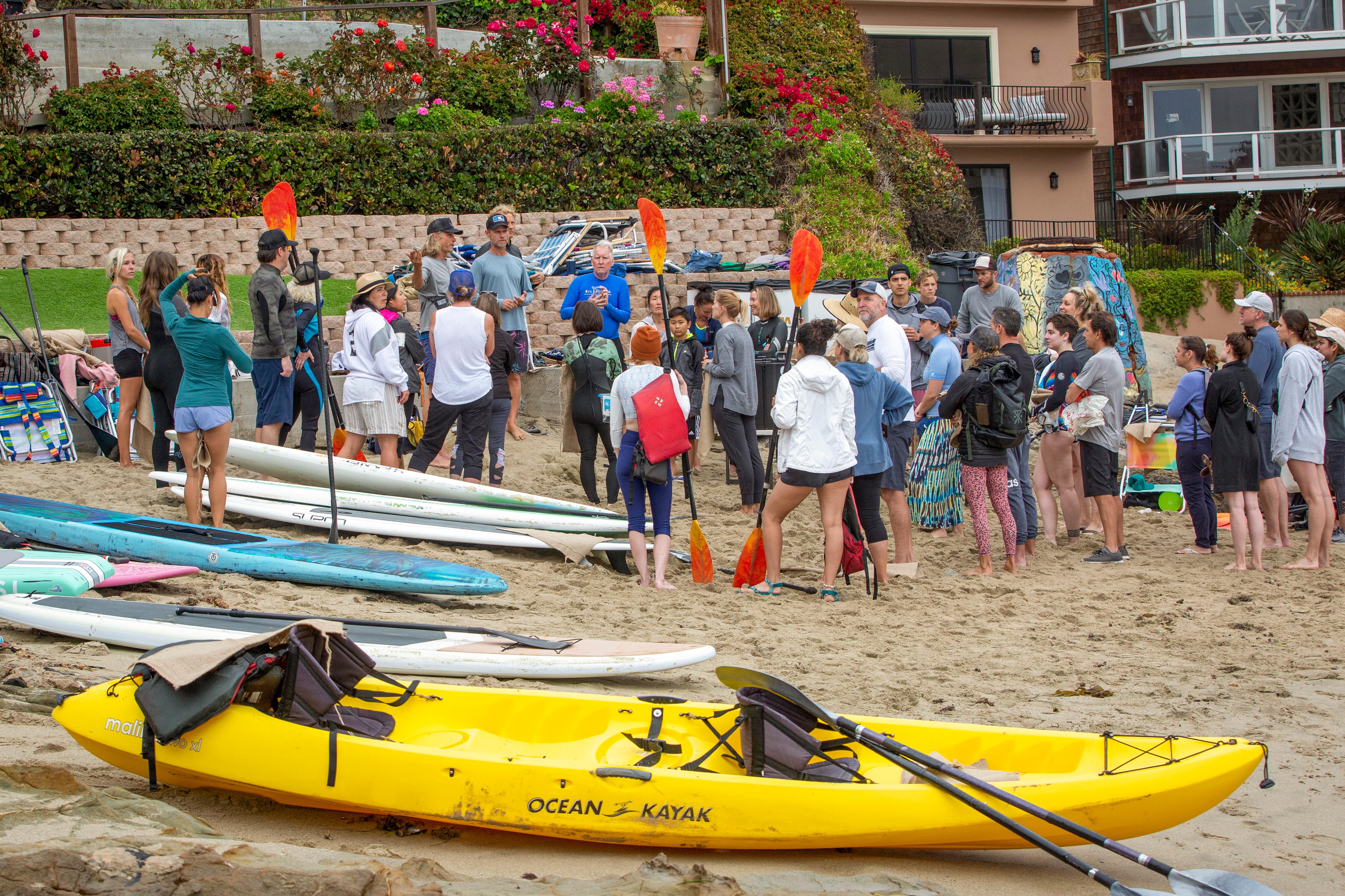 Group gathered on beach with paddleboards and kayaks, team building adventure, Laguna Beach coastal experience