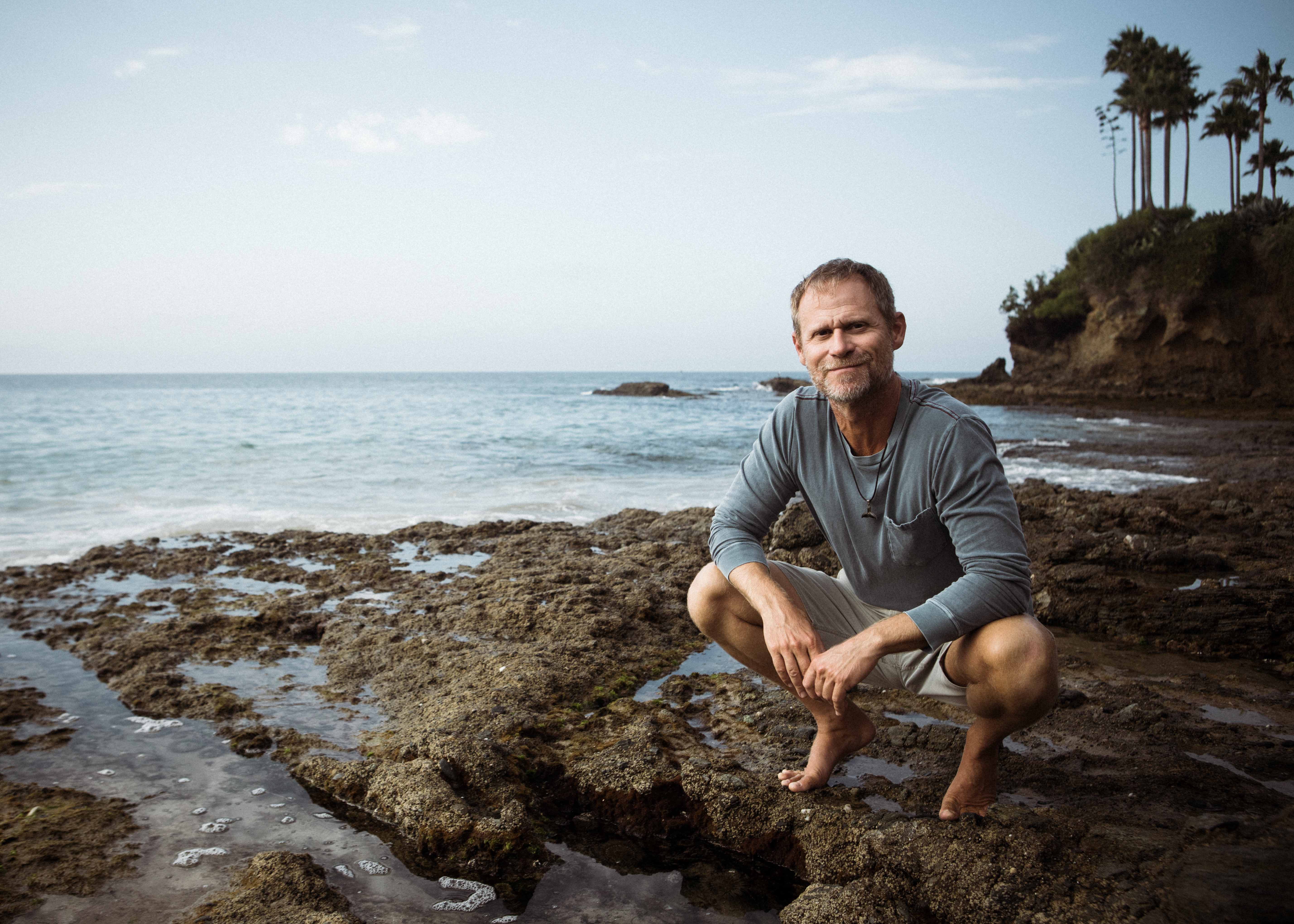 Rich German crouching on rocky Laguna Beach coastline, professional portrait of ocean conservationist and adventure guide